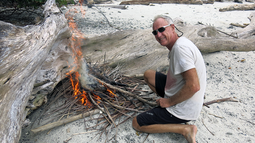 Neil getting a fire going with a glass of rum to hand