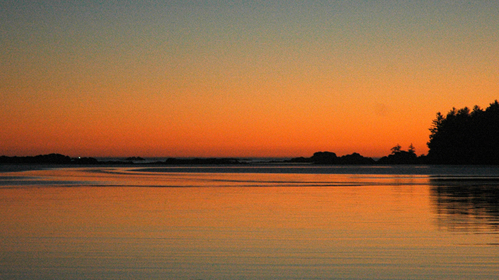The entrance to Nuchatlitz Bay dotted with rocks and islands lit by a scarlet sunset